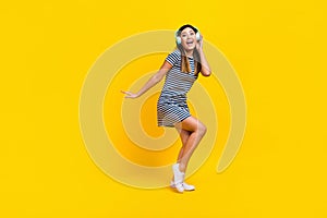 Full length photo of funky cheerful lady wear striped dress dancing listening songs empty space  yellow color