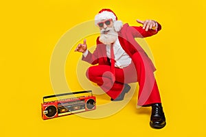 Full length photo of funky cool man pensioner dressed red suit santa hat listening boom box songs isolated yellow color