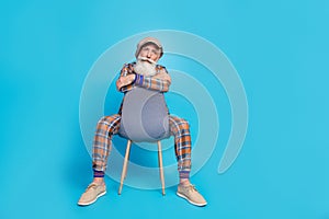 Full length photo of funky cool retired man dressed plaid suit sitting chair empty space isolated blue color background