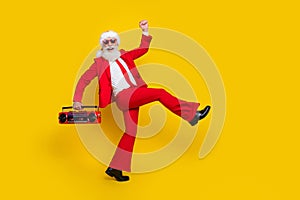 Full length photo of funky cool santa dressed red suit tie enjoying boom box songs walking empty space isolated yellow