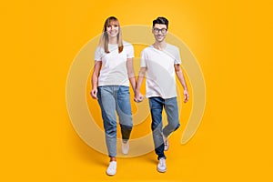 Full length photo of funky cute two persons dressed white t-shirt walking holding hands arms isolated yellow color