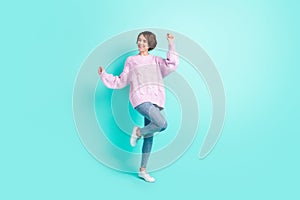 Full length photo of funky cute young woman wear violet sweater dancing rising fists isolated turquoise color background