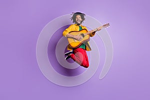 Full length photo of funky dark skin man wear yellow shirt jumping playing guitar isolated violet color background