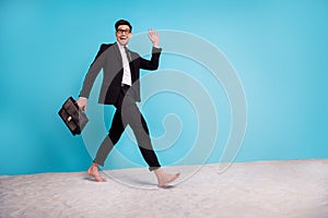 Full length photo of funky friendly man wear black suit spectacles case waking sand beach waving arms empty space