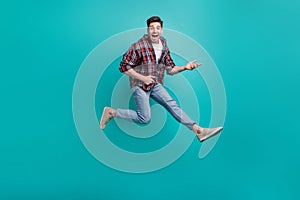 Full length photo of funky good mood guy wear checkered shirt jumping high playing guitar isolated teal color background
