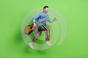 Full length photo of funky positive guy dressed jeans shirt jumping enjoying guitar music running empty space isolated