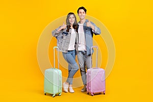 Full length photo of funny charming married couple wear jeans showing thumbs up going new travel isolated yellow color