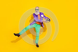 Full length photo of funny cheerful man wear purple velvet jacket dancing holding discotheque ball walking isolated