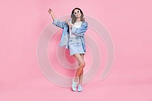 Full length photo of funny funky wavy young woman wear denim outfit dark glasses dancing isolated pink color background