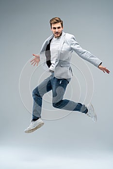 Full-length photo of funny man in casual t-shirt, blazer and jeans running or jumping in air isolated over gray