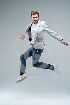 Full-length photo of funny man in casual t-shirt, blazer and jeans running or jumping in air isolated over gray photo