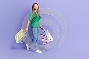 Full length photo of funny positive girl dressed green t-shirt holding bargains walking empty space  purple