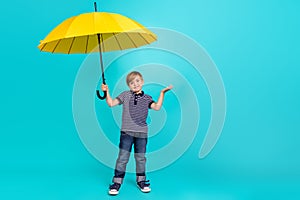 Full length photo of funny small boy hold umbrella wear t-shirt jeans sneakers isolated on teal background