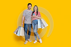 Full length photo of good mood couple with shopping bags in hands clever girl hold smartphone isolated on vivid yellow