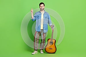 Full length photo of good mood nice guy wear denim jacket playing guitar showing v-sign isolated green color background