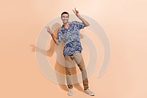 Full length photo of good mood optimistic man dressed blue shirt brown trousers showing v-sign symbol isolated on beige