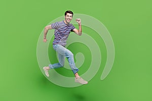 Full length photo of handsome cute man dressed striped t-shirt jumping high running empty space isolated green color