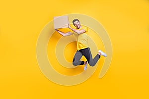 Full length photo of handsome guy jumping high holding big carton box moving to new flat wear casual t-shirt black pants