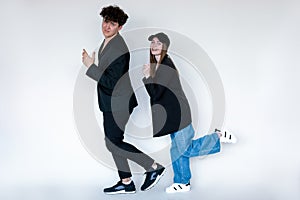 Full length photo of happy couple moving in black blazers, gray studio background. Curly handsome guy posing with pretty
