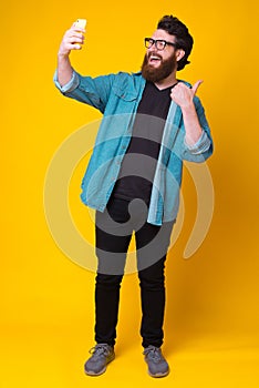 Full length photo of happy man with beard taking selfie over yellow background