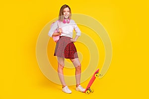 Full length photo of little girl with skate headphones wear shirt skirt bag sneakers isolated on yellow background