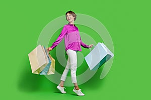 Full length photo of lovely cheerful girl wearing purple clothes carrying packages looking empty space isolated on green