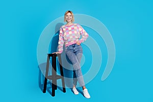 Full length photo of lovely girl wear checkered pullover pants lean on bar chair hold palm in pocket isolated on blue