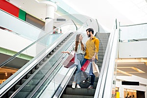 Full length photo of lovely lady handsome guy talking couple spend free time carry many bags moving down escalator