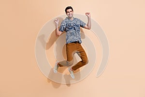 Full length photo of man jumping air raised fists up celebrate victory in international competition isolated over beige