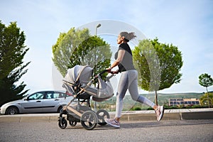 Full length photo in motion of an active woman exercising outdoors, running morning jog while pushing her baby pram