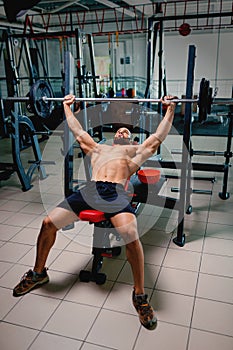 A sports guy doing exercise with a big barbell on a bright gym background. A bodybuilder training in a fitness club.