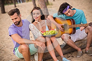Full length photo of nice ladies guys sit eat fruit play guitar wear casual cloth ouside on the beach