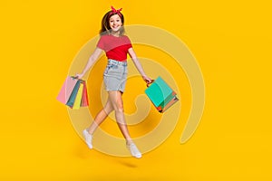 Full length photo of nice teen girl jump with bags wear t-shirt headband skirt footwear isolated on yellow background