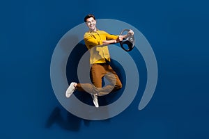 Full length photo of nice young male jumping hold steering wheel dressed stylish yellow garment isolated on dark blue