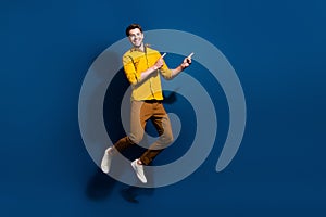 Full length photo of nice young male jumping point empty space dressed stylish yellow garment isolated on dark blue