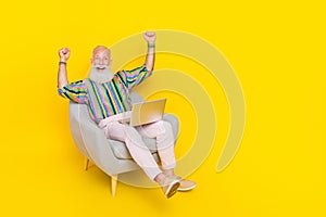 Full length photo of overjoyed positive person sit armchair raise fists gable luck isolated on yellow color background