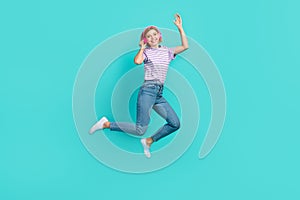 Full length photo of pleasant girl stylish t-shirt denim pants waving hand touching headphones isolated on turquoise