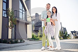 Full length photo of positive adorable family hands hold paper house card toothy smile look camera spend time outdoors