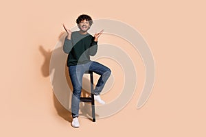 Full length photo of positive impressed guy dressed sweatshirt sitting bar chair emtpy space isolated beige color