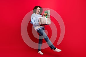 Full length photo of pretty carefree girl dressed ugly christmas sweater walking holding presents pile  red