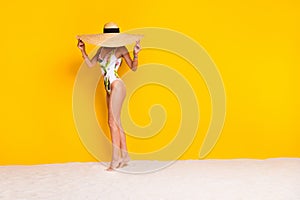 Full length photo of shy sexy lady wear swimsuit walking beach sun headwear cover face empty space isolated yellow color