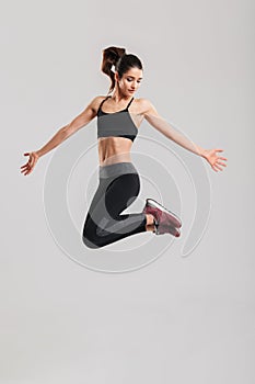 Full-length photo of slim pretty woman in sportswear having strong abdominal muscles jumping and having fun in gym, isolated