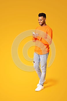 Full length photo of smiling young Indian man texting on the smartphone, using mobile phone for communication online