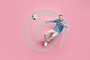 Full length photo of sporty cute young guy wear blue pullover jumping playing football isolated pink color background