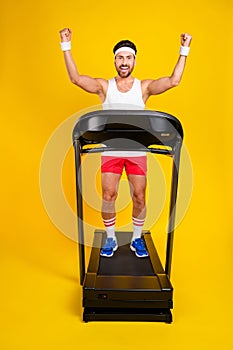 Full length photo of strong cool guy activewear walking treadmill rising fist showing muscles isolated yellow color