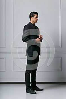 Full length photo of an stylish confident young man in black suit looking in profile, on white background