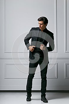 Full length photo of an stylish young man in black suit looking to his side, on white background