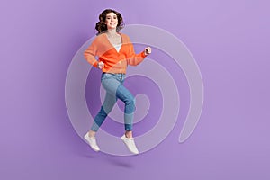 Full length photo of sweet cute woman dressed orange jumping high running fast empty space  purple color