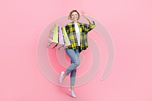 Full length photo of sweet friendly lady wear plaid shirt jumping waving arm holding shoppers isolated pink color