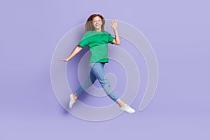 Full length photo of sweet pretty girl dressed green t-shirt jumping high waving palm arm walking isolated purple color